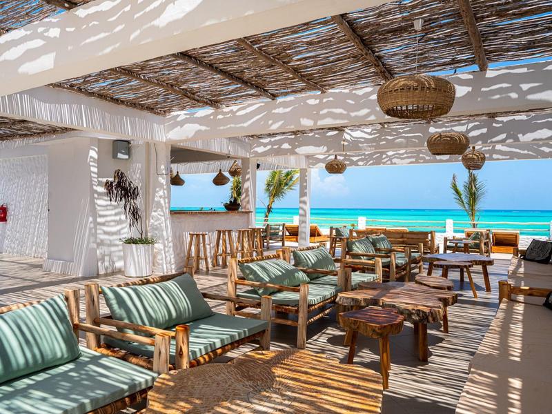 Offener Lounge-Bereich mit Holzmöbeln und Blick auf das Meer unter einem Dach aus Holzlatten.