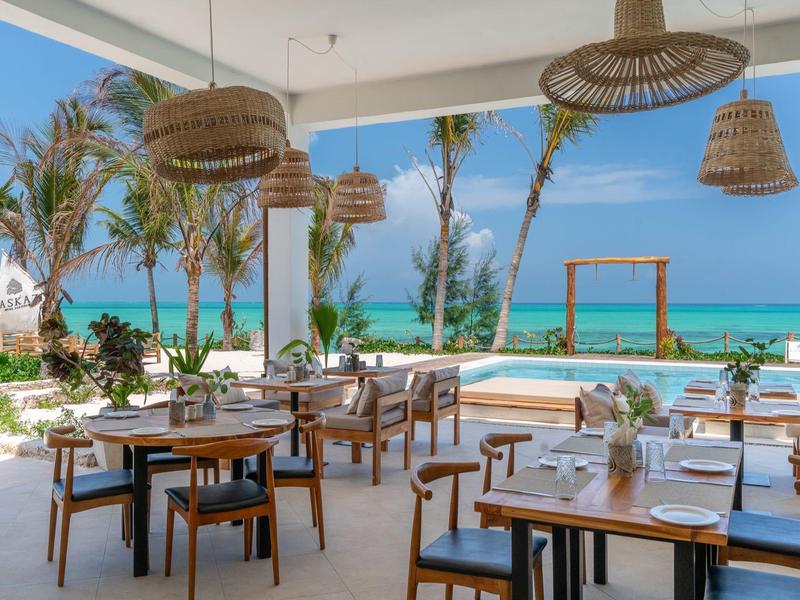 Offenes Restaurant mit Blick auf Palmen, Pool und türkisfarbenes Meer unter blauem Himmel.