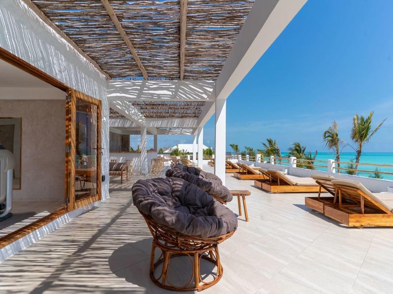 Terrasse mit Korbsesseln und Liegestühlen neben einem Fitnessraum mit Blick auf das Meer.