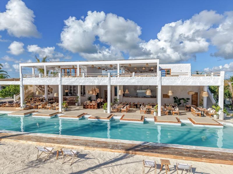 Modernes Hotel mit Pool, Sonnenterrassen und Outdoor-Loungemöbeln unter blauem Himmel.
