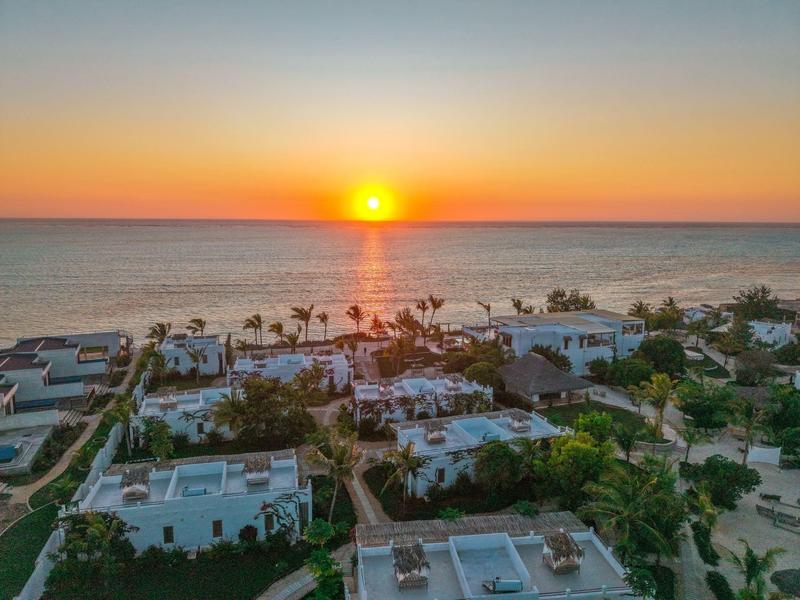 Sonnenuntergang über einer Küstenanlage mit modernen Gebäuden und Palmen am Meer.