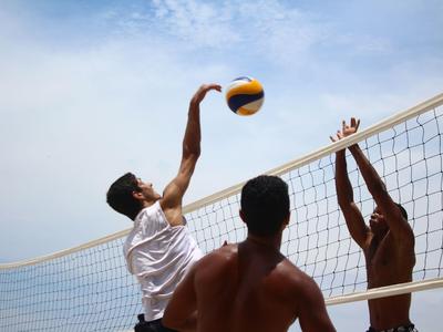 Drei Männer spielen Beachvolleyball unter klarem Himmel am Netz.