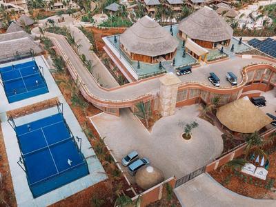 Luftaufnahme eines Hotelkomplexes mit Tennisplätzen, runden Gebäuden und Poolbereich.