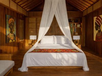 Elegantes Hotelzimmer mit weißem Himmelbett und afrikanischer Kunst an den Holzwänden.