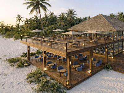 Holzterrasse am Strand mit Tischen, Stühlen und Palmen im Hintergrund bei Sonnenuntergang.