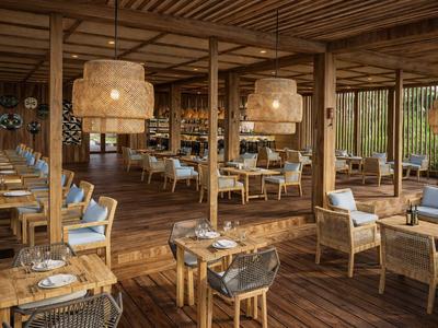 Innenbereich eines Hotels mit hölzernen Möbeln und Deckenlampen, Terrassenfenster im Hintergrund.