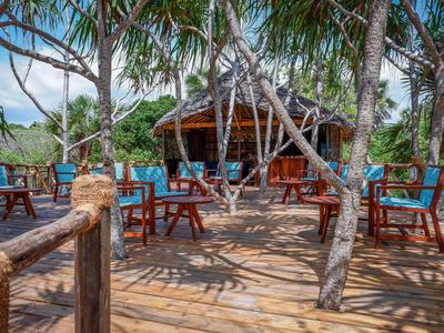 Außenbereich eines Hotels mit Holzboden, Stühlen und Tischen unter Palmen.