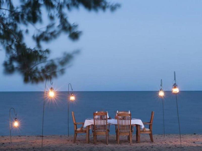 Tavolo romantico sul mare con lanterne appese e cielo serale blu.