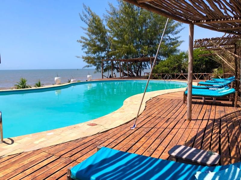 Area piscina con pavimento in legno, sedie a sdraio blu e vista mare con cielo sereno.