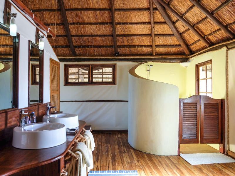 Bagno luminoso con soffitto in legno, doppi lavandini e parete divisoria curva.