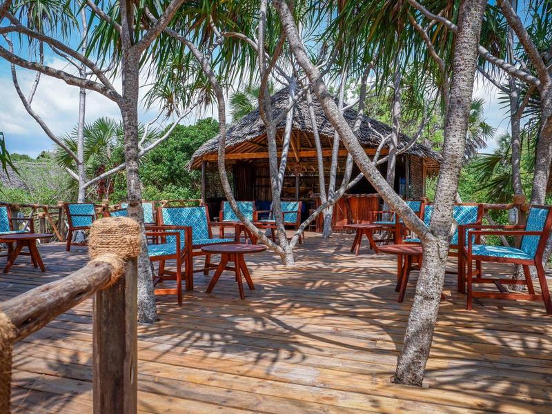 Terrazza in legno con cuscini blu e padiglione ombreggiato sotto palme