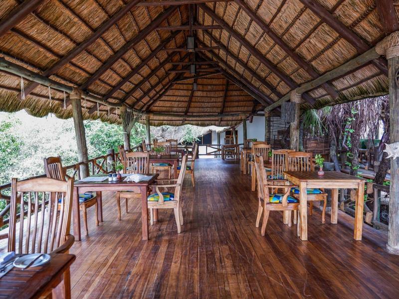 Area pranzo aperta con sedie e tavoli in legno sotto un tetto di paglia.