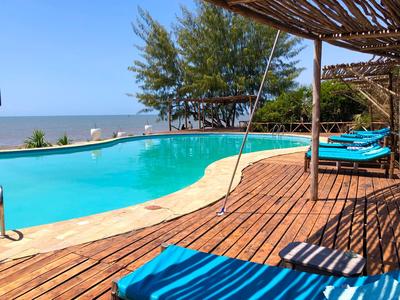 Ein Pool mit türkisfarbenem Wasser neben einer Holzterrasse und Liegestühlen mit Meerblick.