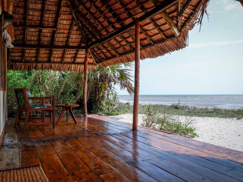 Terraza de madera cubierta con sillas y mesa junto a una playa de arena y vista al mar.