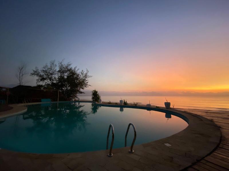 Piscina redonda en la playa al atardecer con mar tranquilo y cielo colorido.