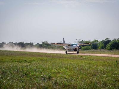 Kleines Flugzeug startet auf Landebahn vor grünem Gras und Bäumen.
