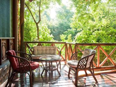 Gemütlicher Balkon mit Holzgeländer, Tisch und drei Stühlen vor grünem Waldhintergrund.