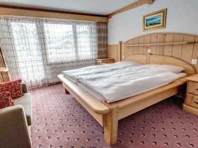 Gemütliches Hotelzimmer mit Doppelbett, Teppichboden und großen Fenstern mit Gardinen.