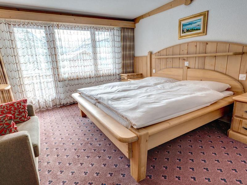 Jasno umeblowany pokój hotelowy z dużym łóżkiem i czerwonym fotelem obok okna z zasłonami.