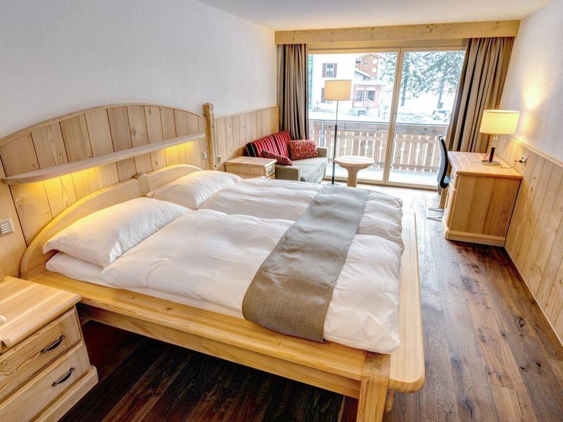 Przytulny pokój hotelowy z łóżkiem dwuosobowym, drewnianą boazerią i balkonem z widokiem na zewnątrz.