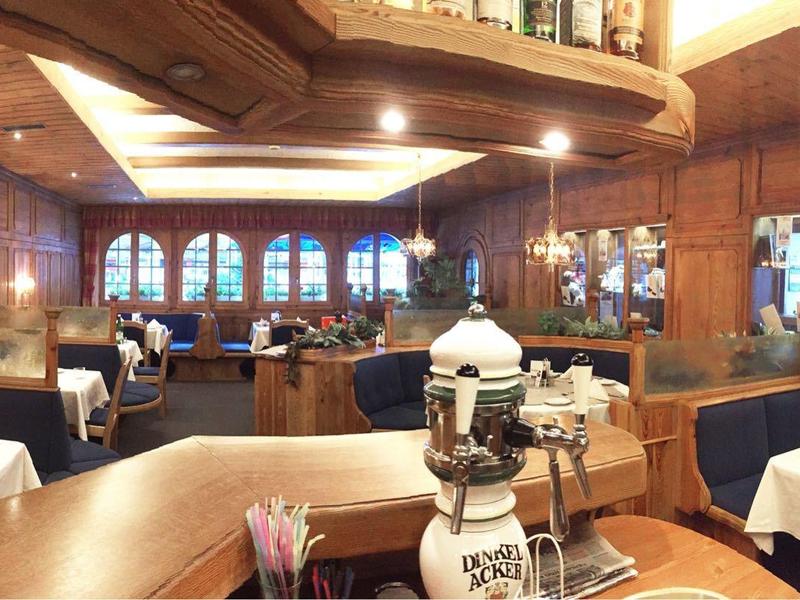 Przytulna część restauracyjna z drewnianymi ścianami, białymi nakrytymi stołami i długim barem.