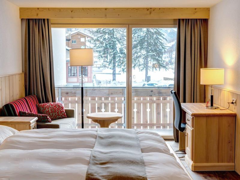 Przytulny pokój hotelowy z dwoma łóżkami, drewnianymi meblami i balkonem z widokiem na góry.