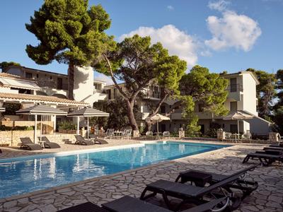 Moderner Hotelpool umgeben von Liegestühlen und mediterranen Bäumen unter blauem Himmel.