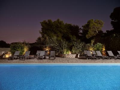 Beleuchteter Pool mit Liegestühlen und Bäumen im Hintergrund bei Nacht.