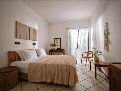 Helles Hotelzimmer mit Doppelbett, Holzmöbeln und einem Fenster mit Vorhängen.