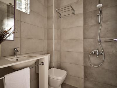 Modernes Bad mit Dusche, Toilette, Waschbecken und großen grauen Fliesen.