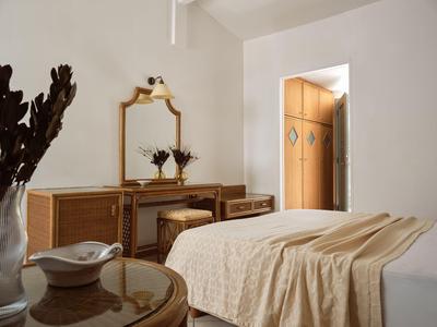Helles Hotelzimmer mit Bett, Holzkommode, Spiegel und minimaler Dekoration.